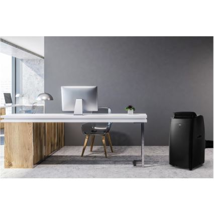 Mobilná klimatizácia stojí v modernej kancelárii s dreveným pracovným stolom, počítačom a stoličkou. Klimatizácia je tmavosivá a umiestnená vedľa pracovného stola.