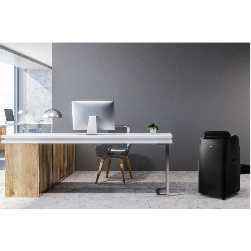 Mobilná klimatizácia stojí v modernej kancelárii s dreveným pracovným stolom, počítačom a stoličkou. Klimatizácia je tmavosivá a umiestnená vedľa pracovného stola.