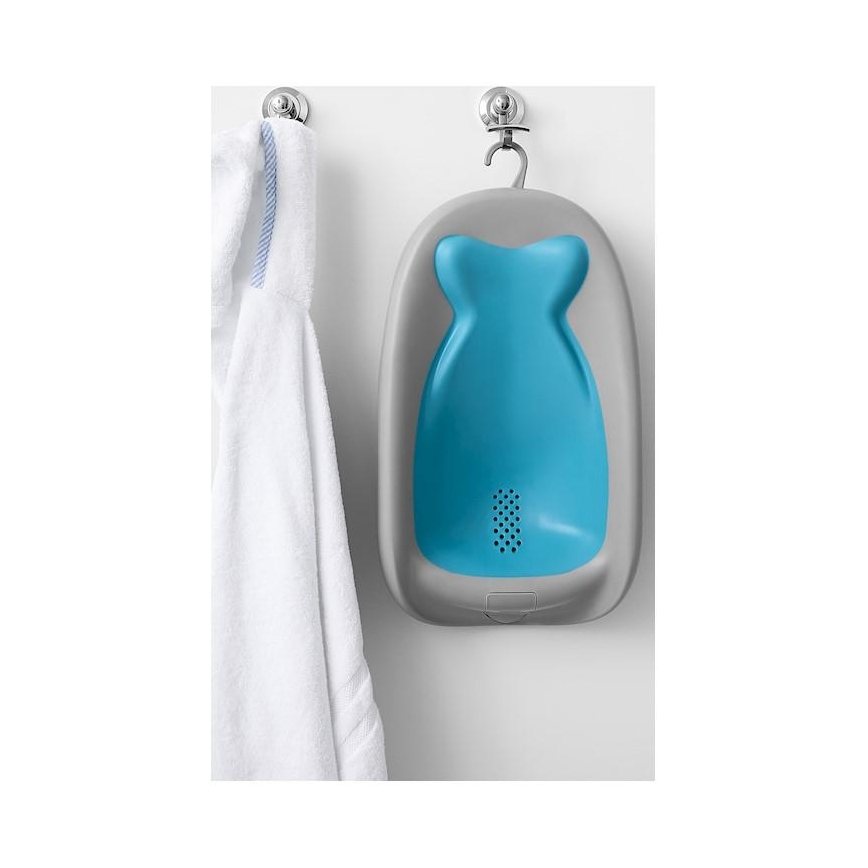 Detská vanička visí na háku na stene. Je svetlomodrej a šedosivej farby. Vedľa nej visí biely uterák.