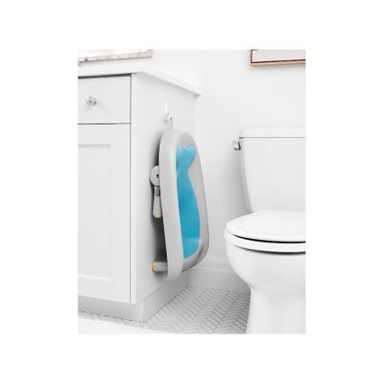 Detská vanička v tvare ryby je zavesená na háčiku na skrinke v kúpeľni. Vanička je svetlosivá s vnútornou modrou časťou. Nachádza sa vedľa toalety.