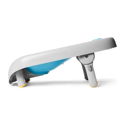 Prebaľovací pult s vaničkou je zobrazený v bočnom profile. Pult je šikmo postavený, má svetlosivú a svetlomodrú farbu a je vybavený nožičkami s protišmykovými koncovkami.