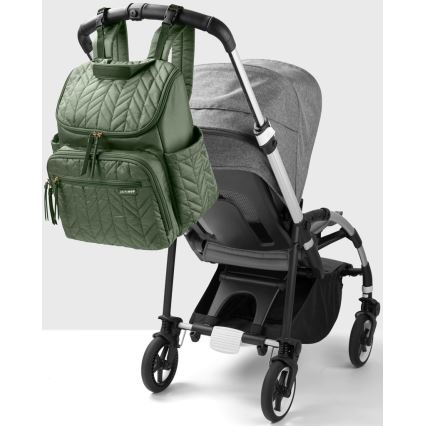 Olivová prebaľovacia taška na batoh je zavesená na kočíku. Taška má prešívaný vzor a zlaté zipsy. Kočík je sivý a čierny, má štyri kolesá a úložný priestor pod sedadlom.