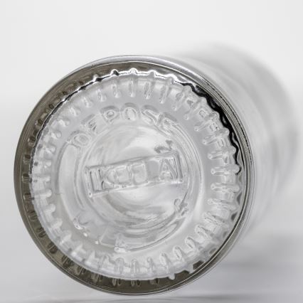 Sklenená fľaša s vyrazeným textom „DEPOSITO“ a „KCUAN“ na dne. Fľaša je obrátená hore dnom. Na svetlom pozadí.