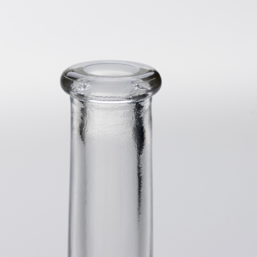 Sklenená fľaša stojí na svetlom pozadí. Je zobrazená horná časť fľaše, s kruhovým otvorom na vrchu. Fľaša je priehľadná.