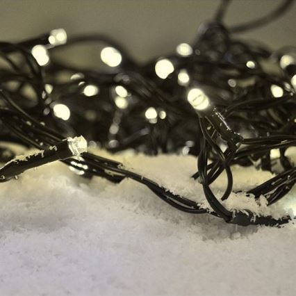 Elektrický svetelný veniec s bielymi LED diódami leží na umelom snehu. Svietiace diódy sú umiestnené na tenkých čiernych kábloch.