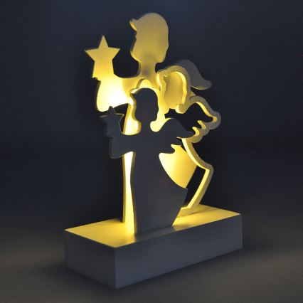 Drevená dekorácia s motívom dvoch anjelov, jeden drží hviezdu, je podsvietená zo zadu. Stojí na bielej podložke.