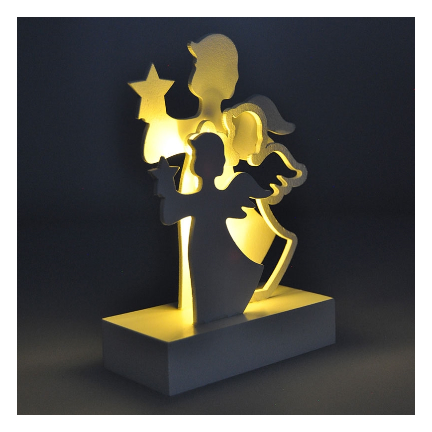 Drevená dekorácia s motívom dvoch anjelov, jeden drží hviezdu, je podsvietená zo zadu. Stojí na bielej podložke.