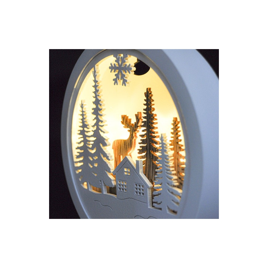 Okrúhla drevená dekorácia zobrazuje jeleňa v zasneženej lesnej scéne s domčekom a smrekovými stromami, podsvietené vnútorným osvetlením. Snehová vločka je umiestnená v hornej časti.