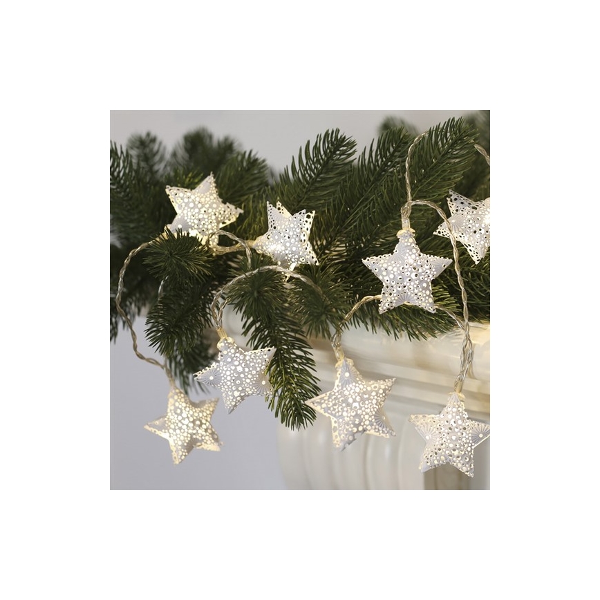 Svetlíková reťaz s hviezdami svieti. Hviezdy sú kovové, striebornej farby, s prepracovaným vzorom. Reťaz je umiestnená na smrekových konároch v kvetináči.