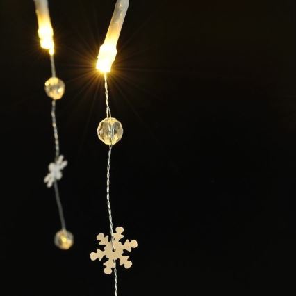 Svetelný reťaz s LED diódami a ozdobnými snehovými vločkami a guličkami visí na tmavom pozadí. Diódy svietia.