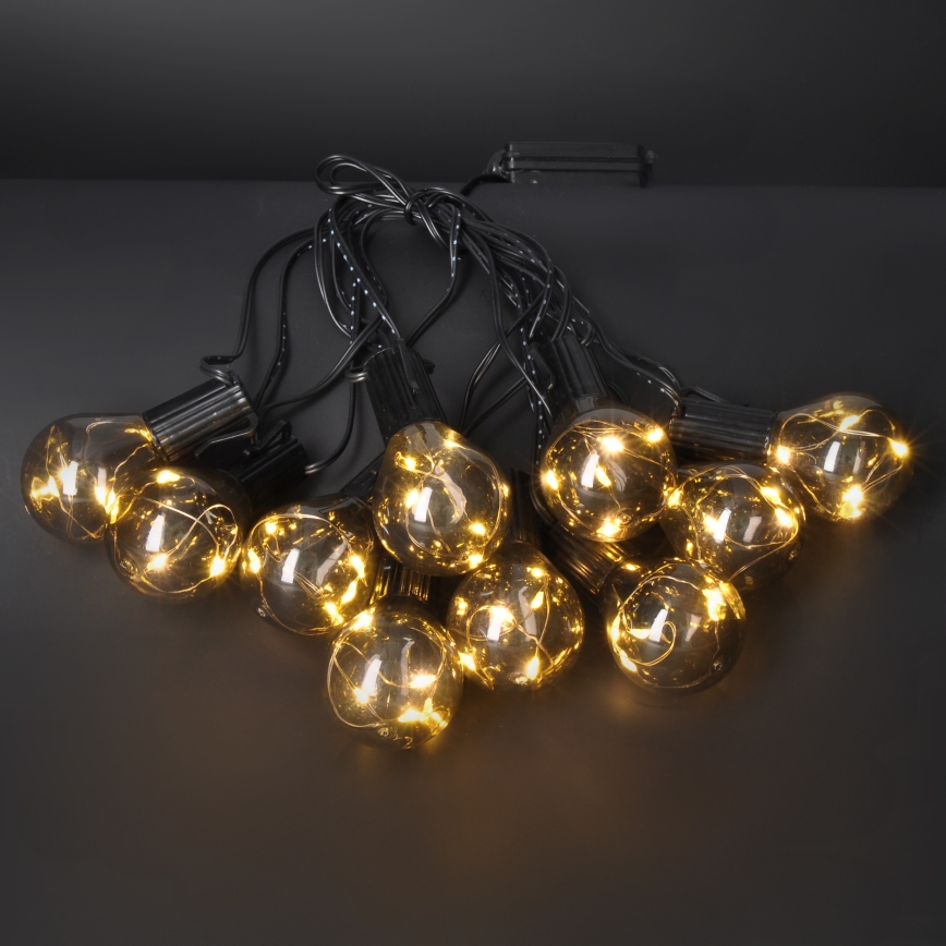 Svetlá svietia. Dvanásť tmavých sklenených žiaroviek na čiernych kábloch je zoskupených na tmavom povrchu. Žiarovky vyžarujú teplé žlté svetlo.