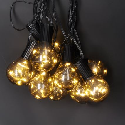 Svietiace guľové LED žiarovky na čiernom kábli visia zhora. Žiarovky svietia teplým žltým svetlom. Tmavosivé pozadie.