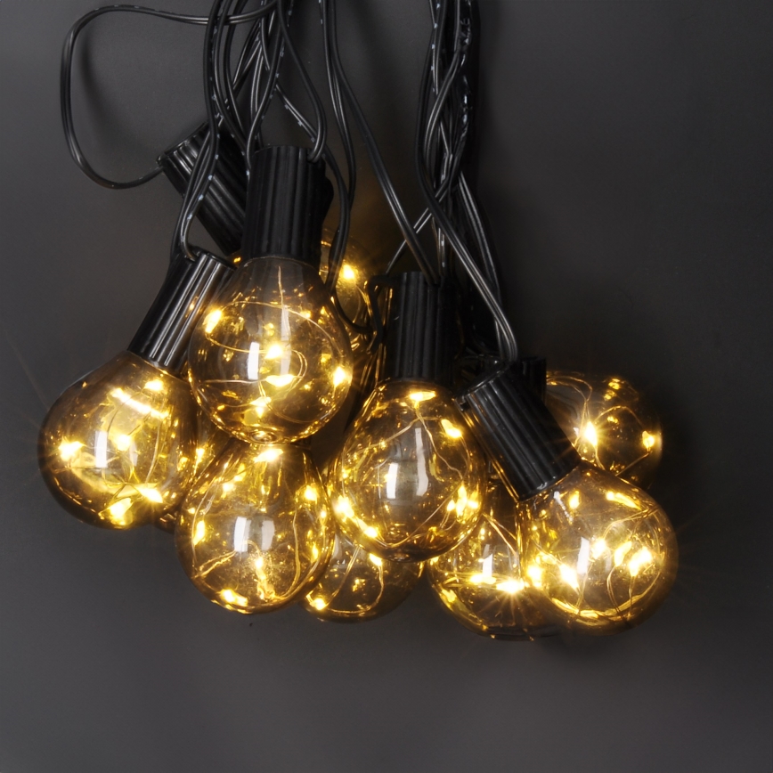 Svietiace guľové LED žiarovky na čiernom kábli visia zhora. Žiarovky svietia teplým žltým svetlom. Tmavosivé pozadie.