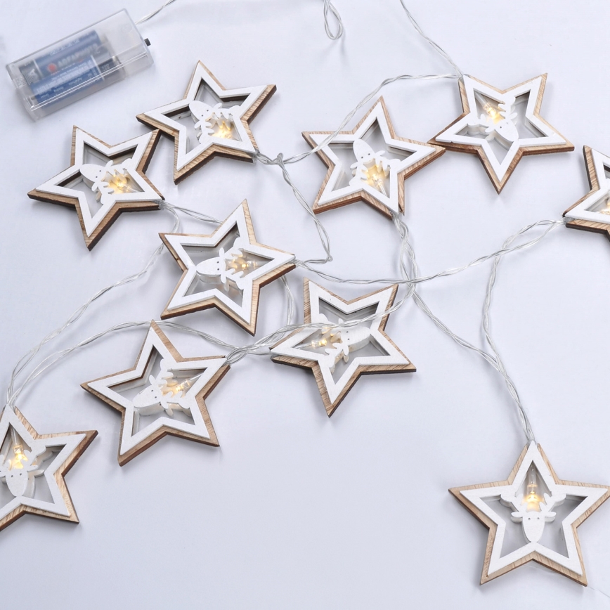Svetlá vo forme drevených hviezd s vyrezávanými sobičkami svietia. Sú rozložené na svetlom pozadí. Batéria je pripojená k svetelnému reťazcu.