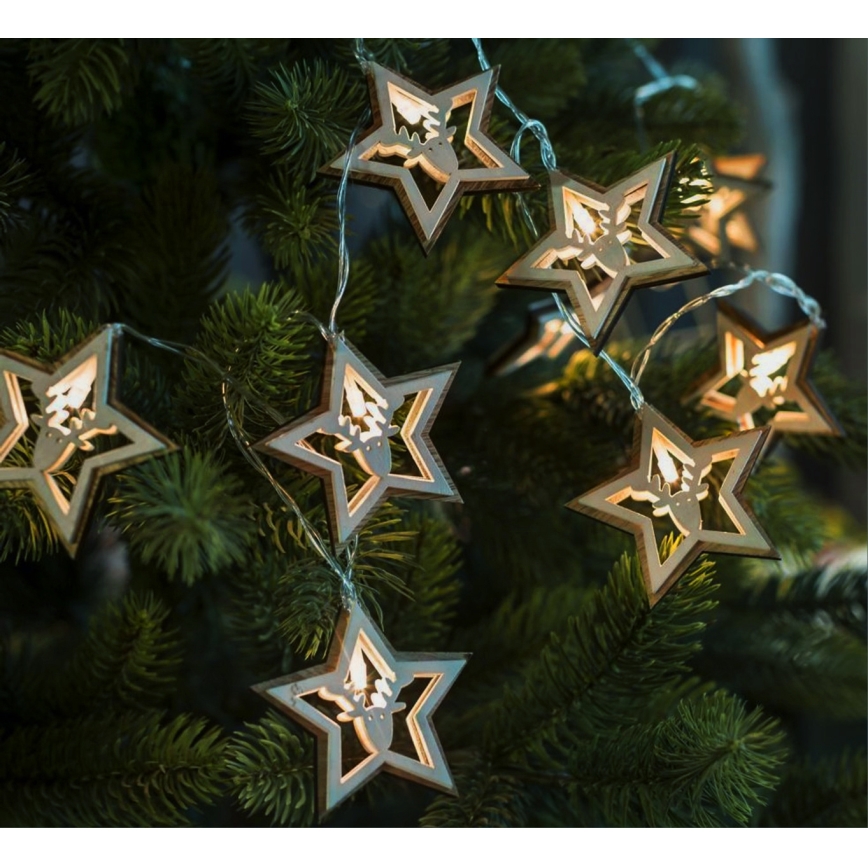 Svetlíka s drevenými hviezdami s vyrezávaným jeleňom svieti na vianočnom stromčeku. Hviezdy sú svetlohnedé a LED diódy v nich svietia teplým svetlom.