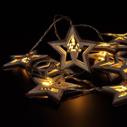 Drevené hviezdy s vyrezávaným jeleňom svietia na šnúrke svetielok. Svietiace hviezdy sú rozprestreté na tmavom povrchu.