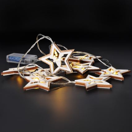 Svetlený veniec s drevenými hviezdami s vyrezávanými motívmi svieti na tmavom povrchu. Hviezdy sú spojené tenkým káblom s batériovým zdrojom.
