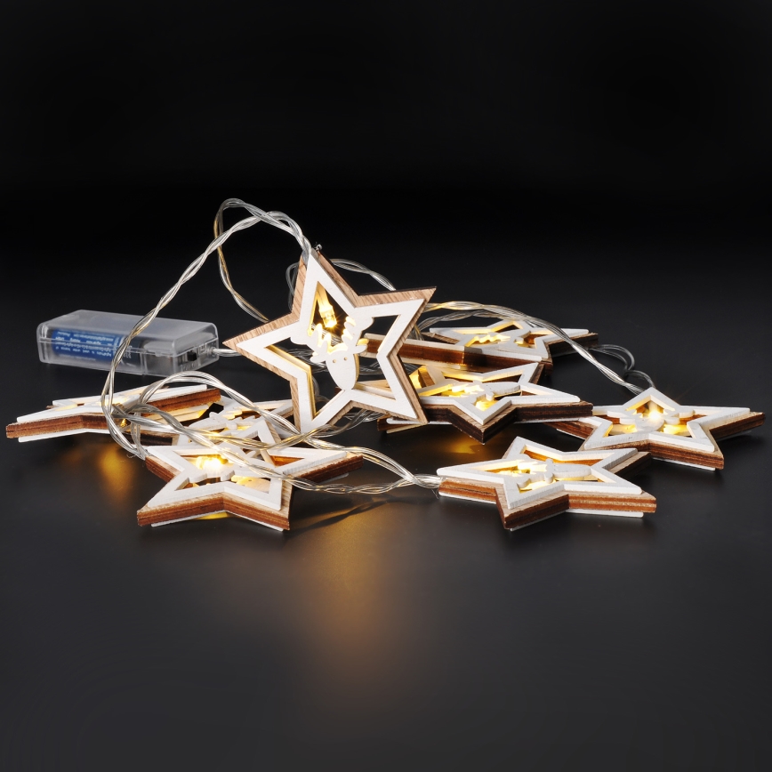 Svetlený veniec s drevenými hviezdami s vyrezávanými motívmi svieti na tmavom povrchu. Hviezdy sú spojené tenkým káblom s batériovým zdrojom.