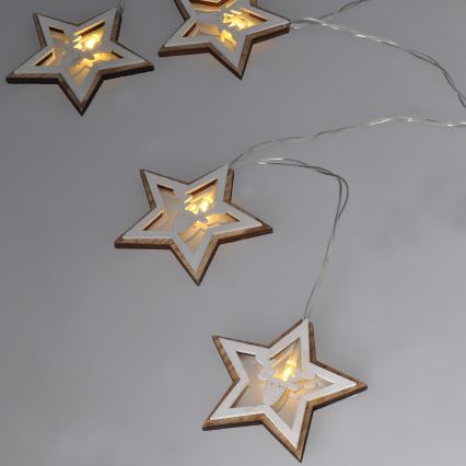 Svetlá v tvare hviezd s vyrezávanými sobmi svietia. Drevené hviezdy sú biele s hnedým okrajom. Sú pripevnené k tenkému drôtu na svetlom sivom pozadí.