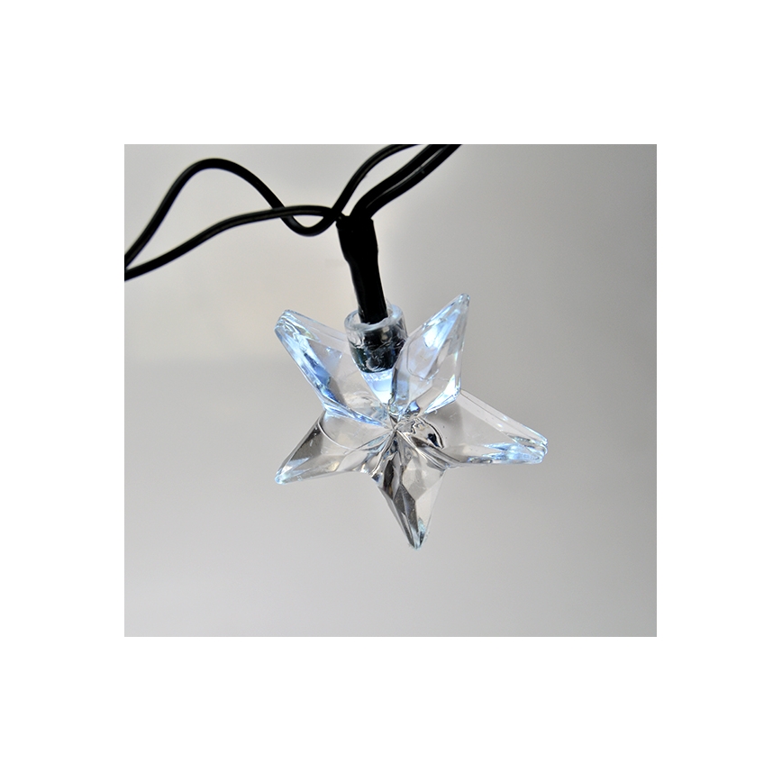 Hviezdická LED dióda visí na čiernom kábli. Svietiaci element je umiestnený v priehľadnej hviezdicovitej ozdobe. Pozadím je svetlosivá plocha.