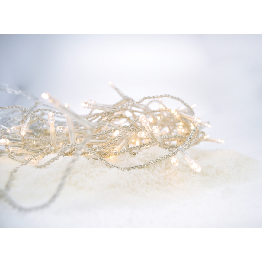 Svetelná reťaz s malými žiarovkami leží na umelom snehu. Žiarovky svietia slabým svetlom. Reťaz je zložená a rozložená na ploche.