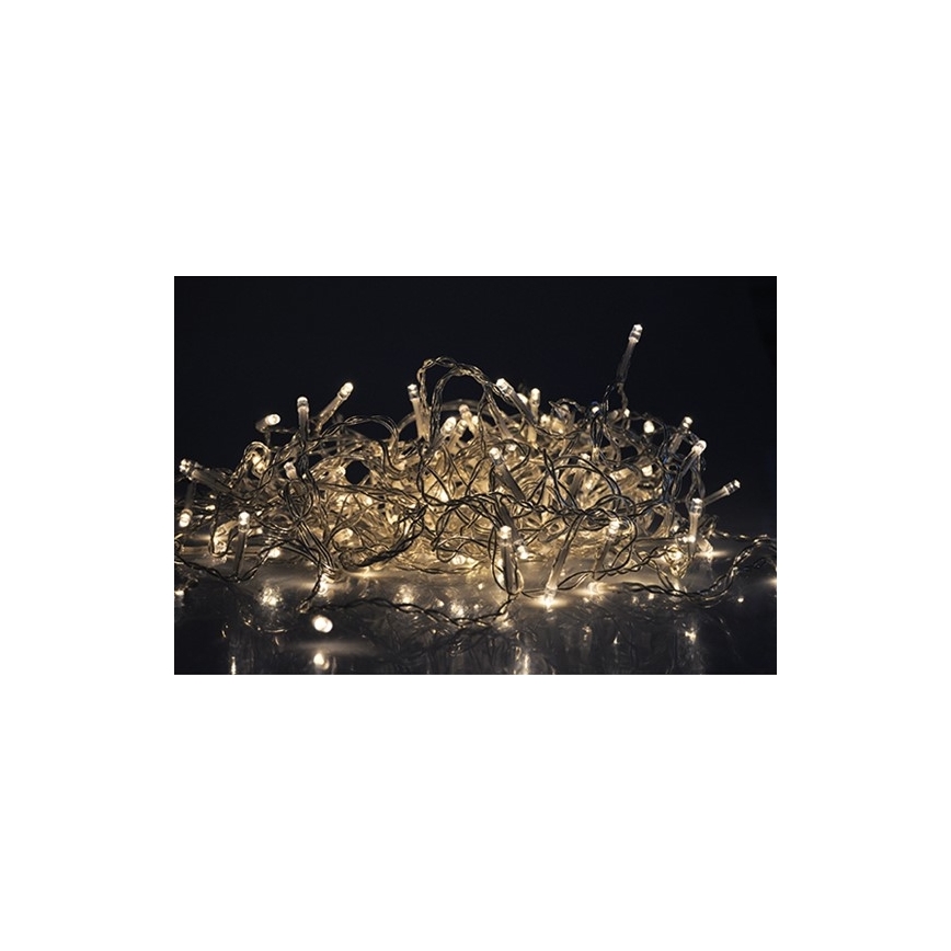 Elektrický svetelný pás s malými žiarovkami s teplým bielym svetlom leží zväčša zmuchlaný na tmavom podklade. Svetlá svietia.