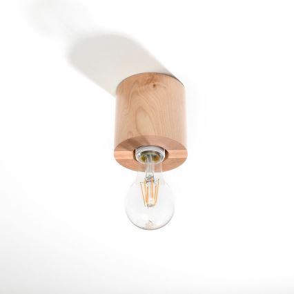 Drevená stropná lampa drží žiarovku. Lampa je z ľahkého dreva, valcovitého tvaru. Je pripevnená k stropu na bielom pozadí.