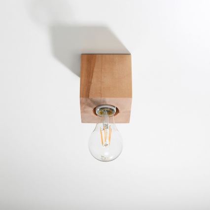 Drevená lampa svieti. Je pripevnená k stropu. Žiarovka je osvetlená.