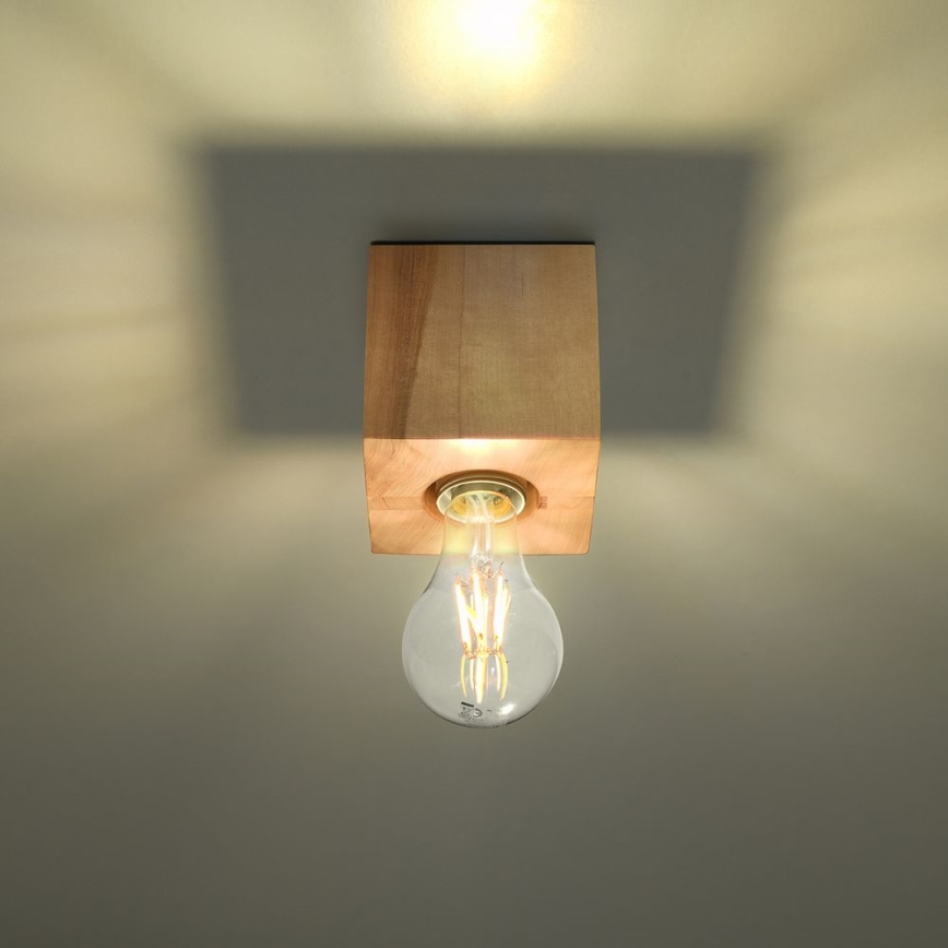 Drevená lampa svieti. Žiarovka je umiestnená v kubickej drevenej konštrukcii pripevnené k stropu. Svetlo svieti.