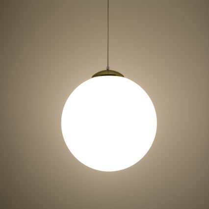 Guľová lampa visí zo stropu. Svieti. Stena je svetlohnedá.