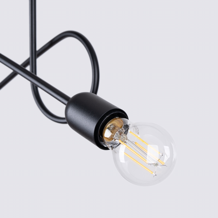 Čierna kovová lampa s vlnovkou v tvare drôtu drží žiarovku. Žiarovka je sklenená s viditeľnými vnútornými vláknami. Pozadí je svetlosivé.