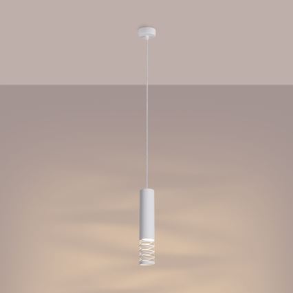 Biela valcová závesná lampa svieti. Je zavesená na tenkom kábli z bieleho stropu v svetlohnedej miestnosti. Lampa má okolo svetelného zdroja ozdobný kovový prvok.