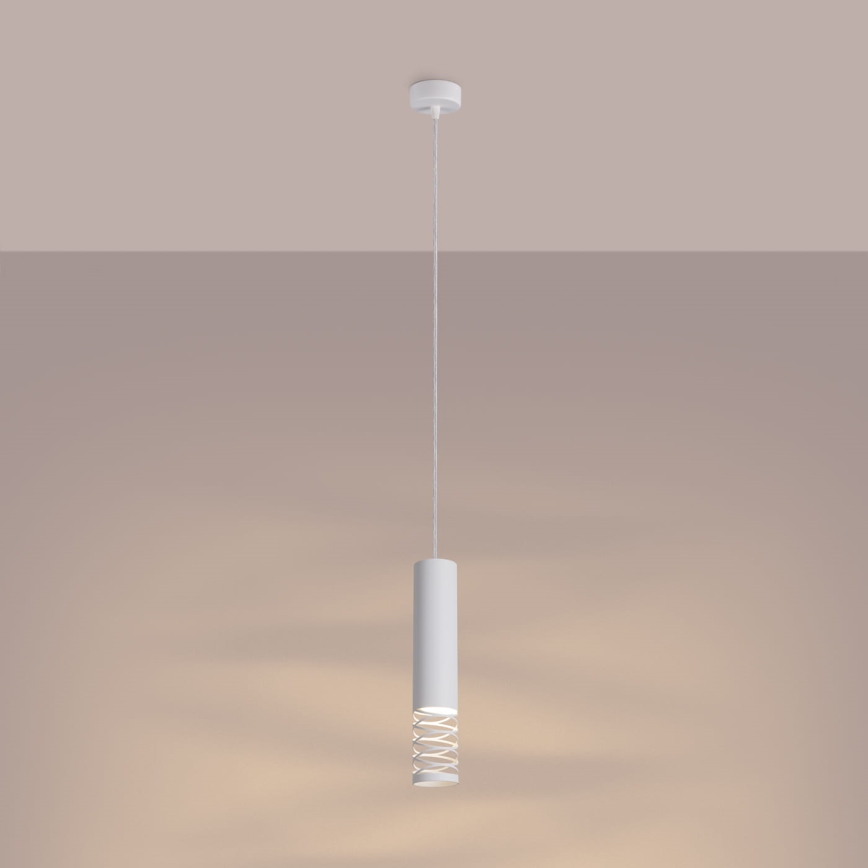 Biela valcová závesná lampa svieti. Je zavesená na tenkom kábli z bieleho stropu v svetlohnedej miestnosti. Lampa má okolo svetelného zdroja ozdobný kovový prvok.