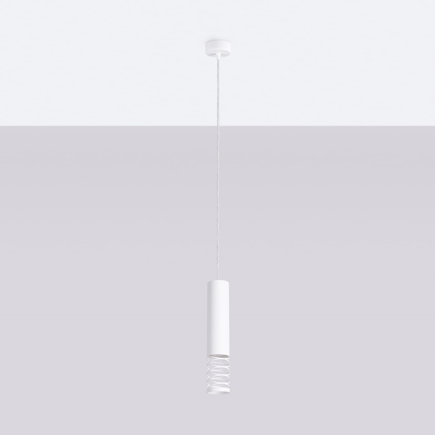 Biela závesná lampa visí zo stropu. Lampa má valcovitý tvar s dekoratívnym pružinovým prvkom. Je umiestnená pred svetlosivou stenou.