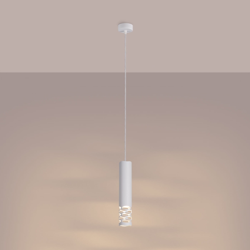 Biela valcovitá závesná lampa s otvormi v strede svieti. Je zavesená na šnúrke z bieleho stropu na svetlohnedom pozadí.