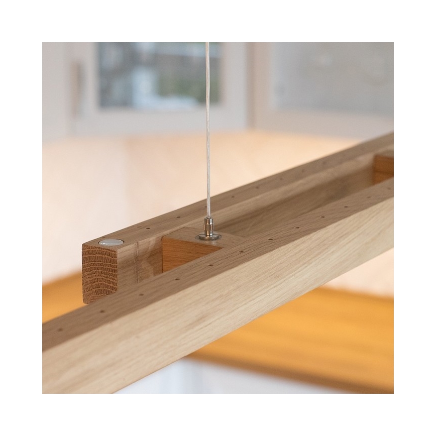 Drevené svietidlo visí zo stropu. Je pripevnené tenkým káblom. Svietidlo je umiestnené v kuchyni.