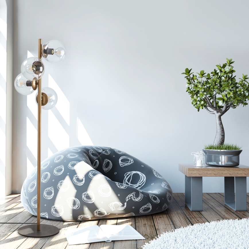 Stojacia lampa s viacerými sklenenými tienidlami stojí pri bezobalovom sedaciemu vaku s abstraktným vzorom. Vedľa je bonsai stromček na drevenom stolíku.