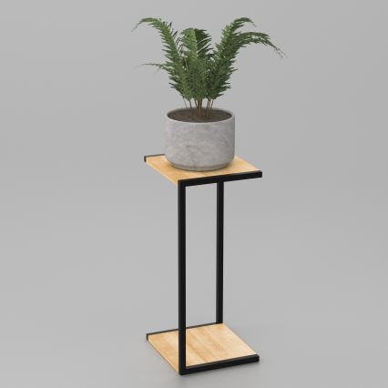 Rastlina v sivom kameninovom kvetináči stojí na drevenom stolíku s čiernym kovovým rámom. Stolík má dve drevené police. Prostredie je jednoduché, svetlosivé pozadie.