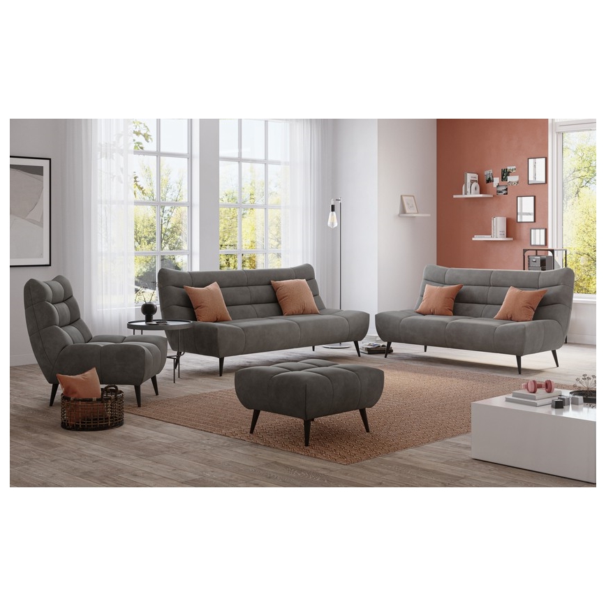 Sivá sedacia súprava, pozostávajúca z trojmiestnej a dvojmiestnej pohovky a kresla, je umiestnená v obývacej izbe na koberci. Súčasťou súpravy je aj taburetka. V pozadí sú okná, stena s poličkou a stolík.