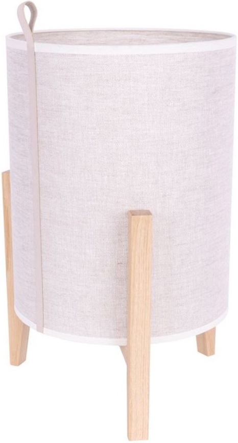 Stolová lampa stojí na štyroch drevených nožičkách. Je vyrobená z béžovej látky a má kožený popruh. Lampa je umiestnená na bielom pozadí.