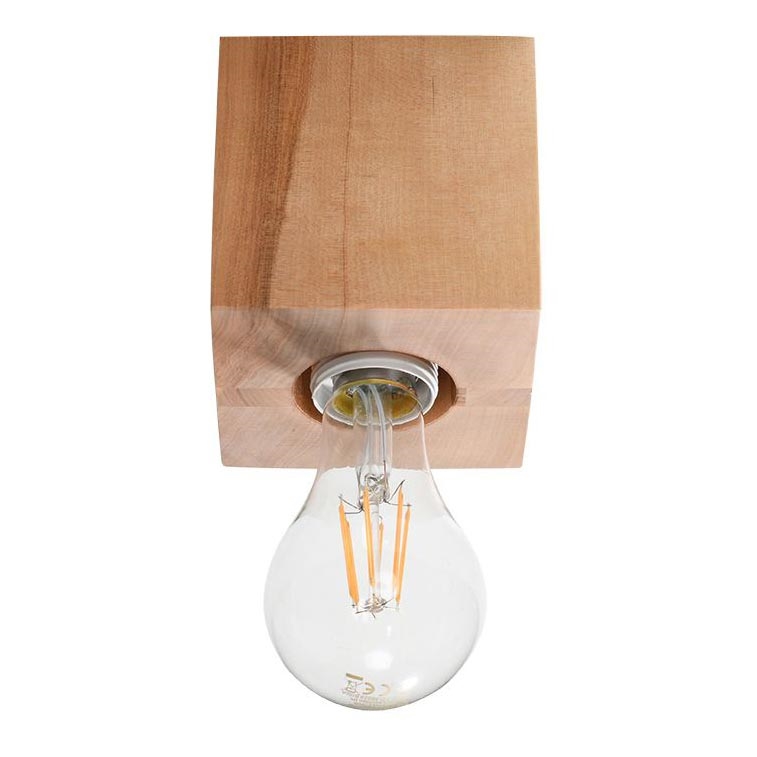 Drevená lampa svieti. Je umiestnená na bielom pozadí. Lampa má tvar kocky z dreva s vyrezaným otvorom pre žiarovku.