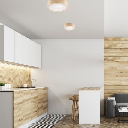 Drevené stropné svietidlá osvetľujú modernú kuchyňu s drevenými a bielymi skrinkami, stoličkami a barovým pultom. Kuchyňa je v priestore s drevenou stenou a dlažbou.