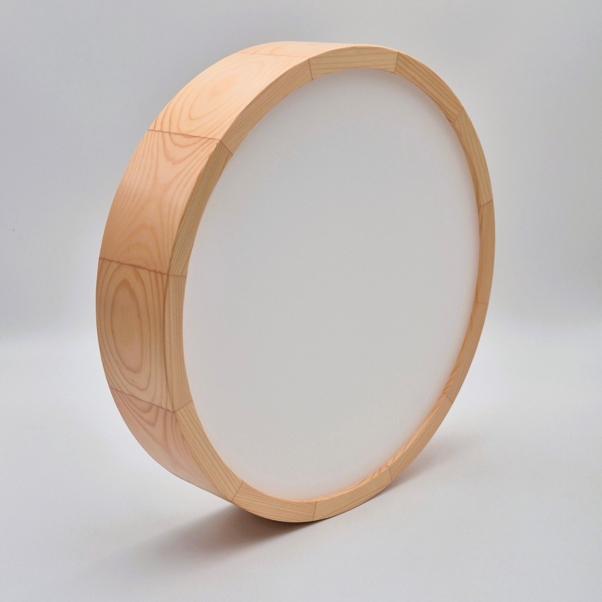 Okrúhle drevené svietidlo s bielym difúzorom je umiestnené na svetlom pozadí. Svietidlo je vyrobené z dreva svetlej farby.