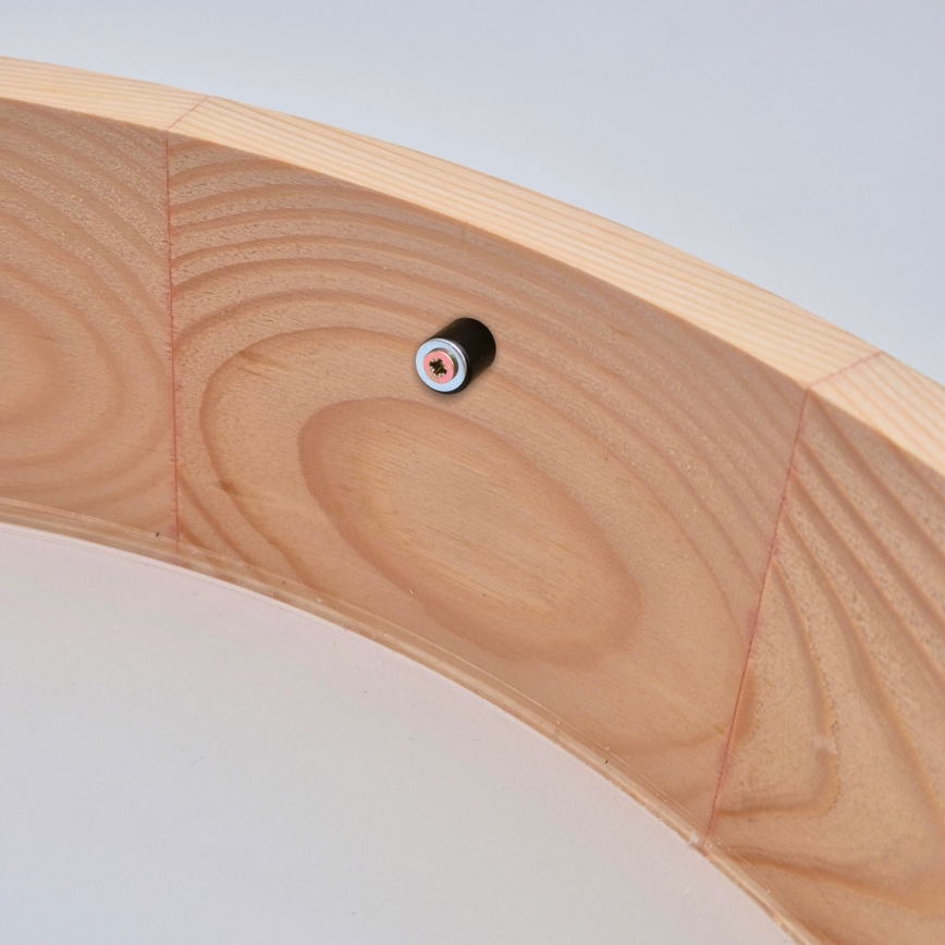 Drevený kruh, do ktorého je pripevnený malý čierny skrutkový diel, je položený na svetlom povrchu.