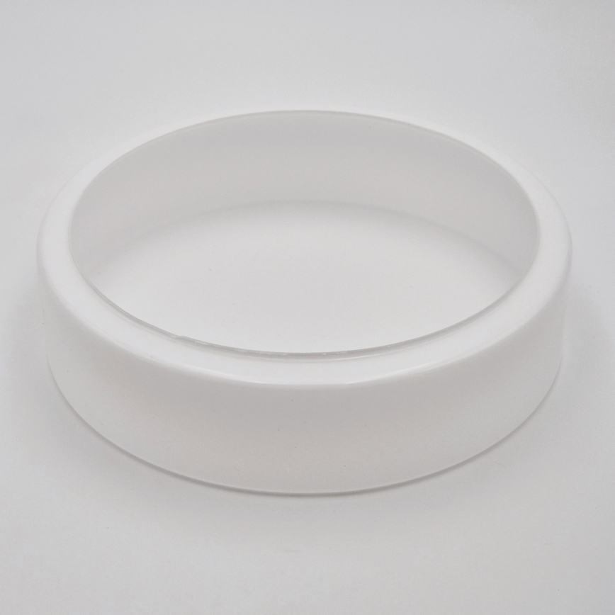 Biela okrúhla nádoba s priehľadným vnútorným okrajom leží na svetlom podklade. Nádoba je položená, nič sa v nej nenachádza.