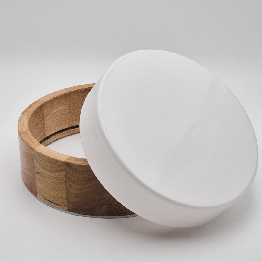 Drevená nádoba s okrúhlym bielym viečkom je otvorená. Nádoba je z svetlého dreva, viečko je hladké a biele. Nachádza sa na bielom pozadí.