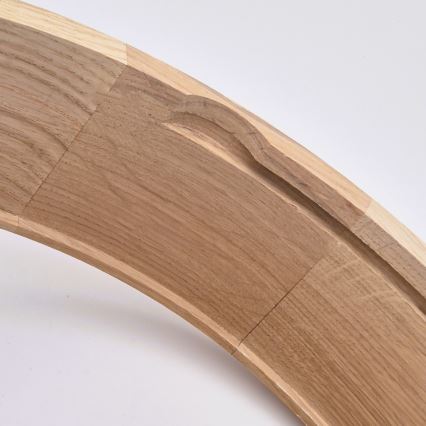 Drevený oblúk, zložený z niekoľkých segmentov, zobrazuje vyrezávaný detail na vnútornej strane. Segmenty sú spojené, viditeľné sú stopy po spracovaní dreva. Svetlé drevo je umiestnené na svetlom pozadí.