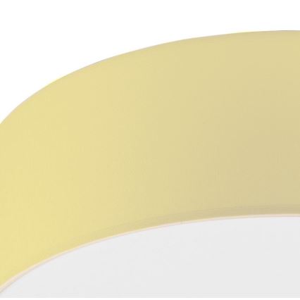 Svetlo s bledžltým tienidlom v tvare mierne prehnutého disku je zobrazené zblízka. Tienidlo je z látky. Pozornosť sa sústreďuje na textúru a farbu tienidla.