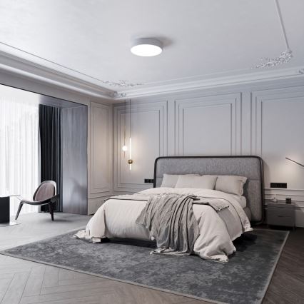 Dvojposteľ stojí v priestrannej spálni. Na posteli je prehodená deka. Spálňu zdobia štukové stropy a steny s lištami.