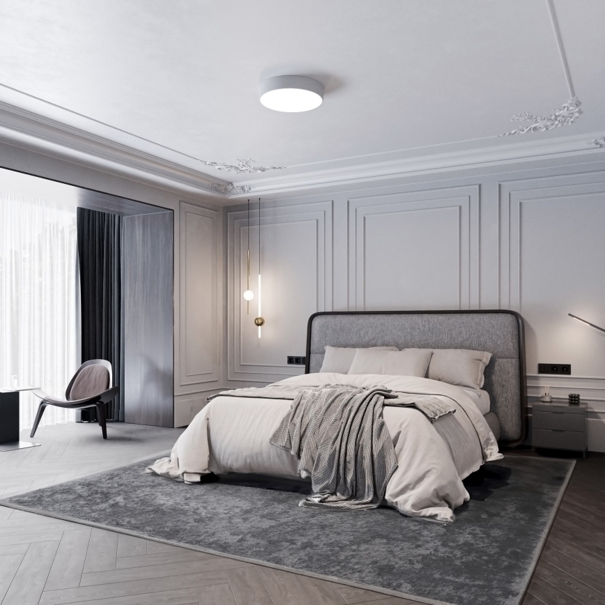 Dvojposteľ stojí v priestrannej spálni. Na posteli je prehodená deka. Spálňu zdobia štukové stropy a steny s lištami.